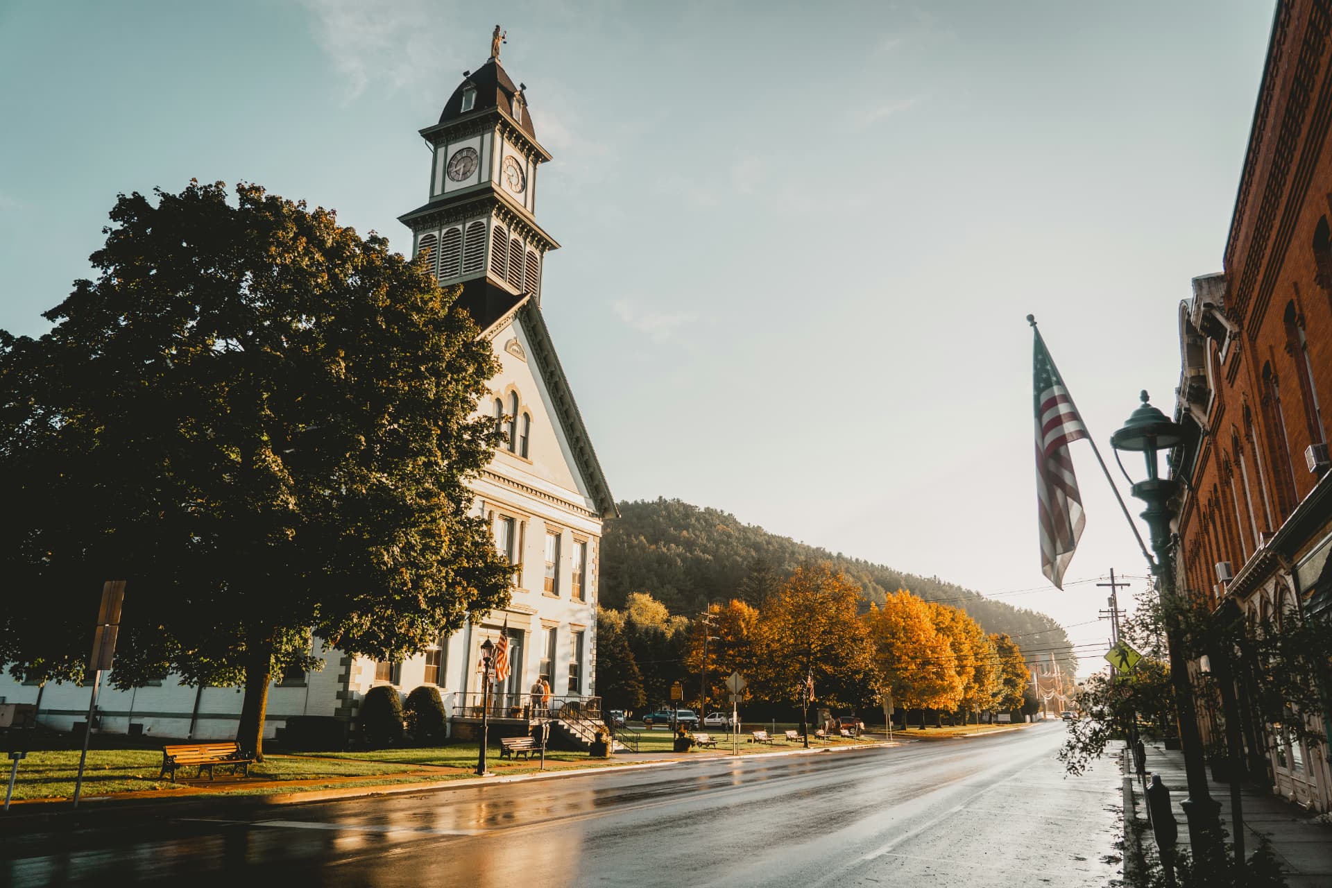 A sunlit American small-town main street lined with historic buildings and a tall clock tower at the center.
